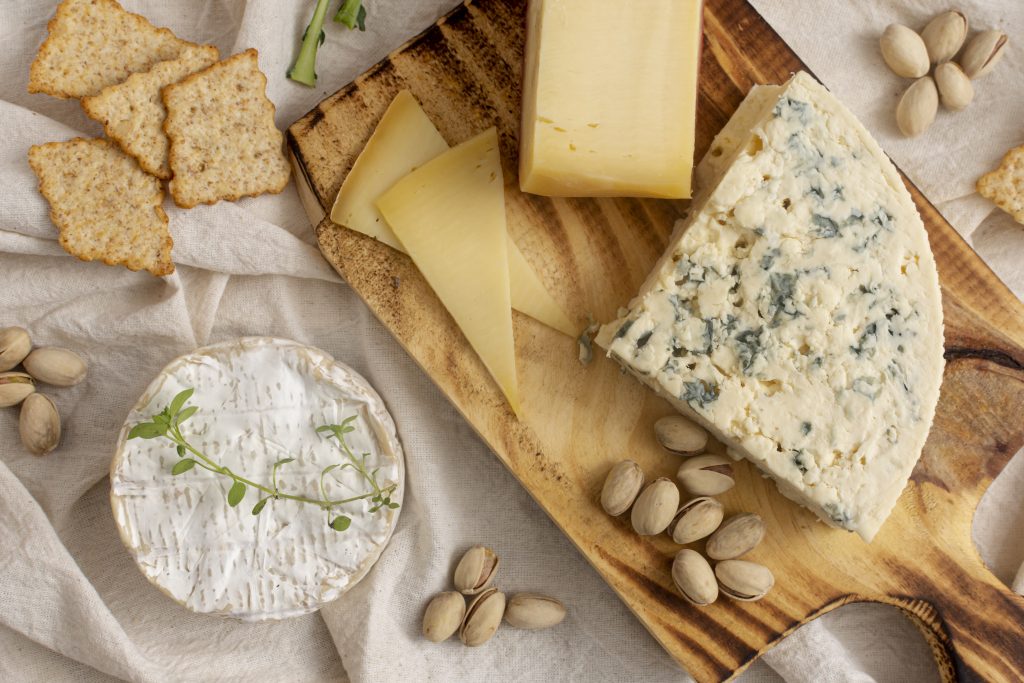 variété de fromages et snacks sur fond de planche à découper en bois et nappe beige froisée